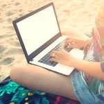 Persona seduta che utilizza computer in spiaggia
