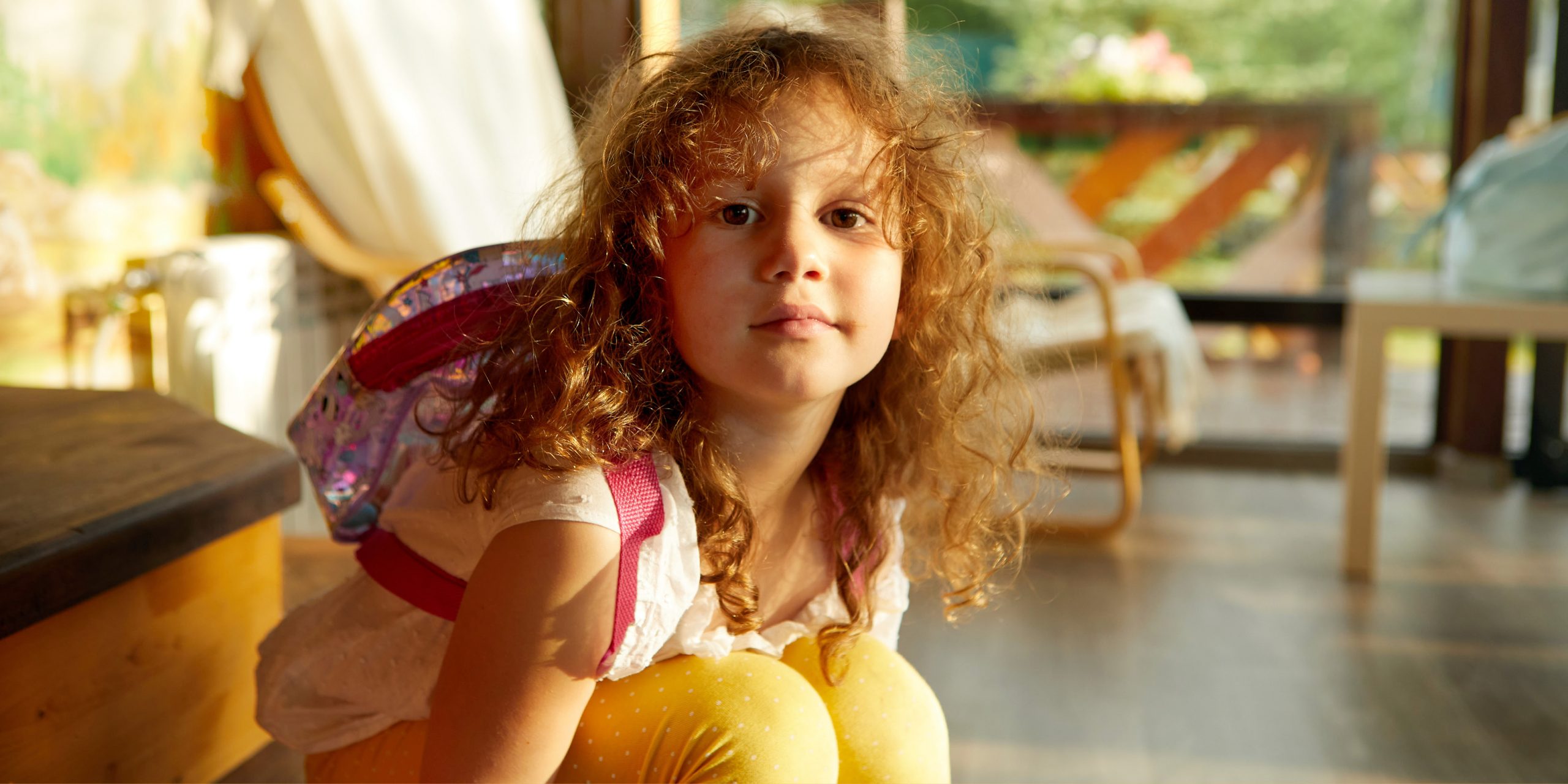 Bambina riccia dai capelli rossi con zaino sulle spalle seduta per terra