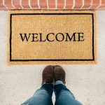 Piedi ripresi dall'alto di fronte ad uno zerbino con su scritto "Welcome"
