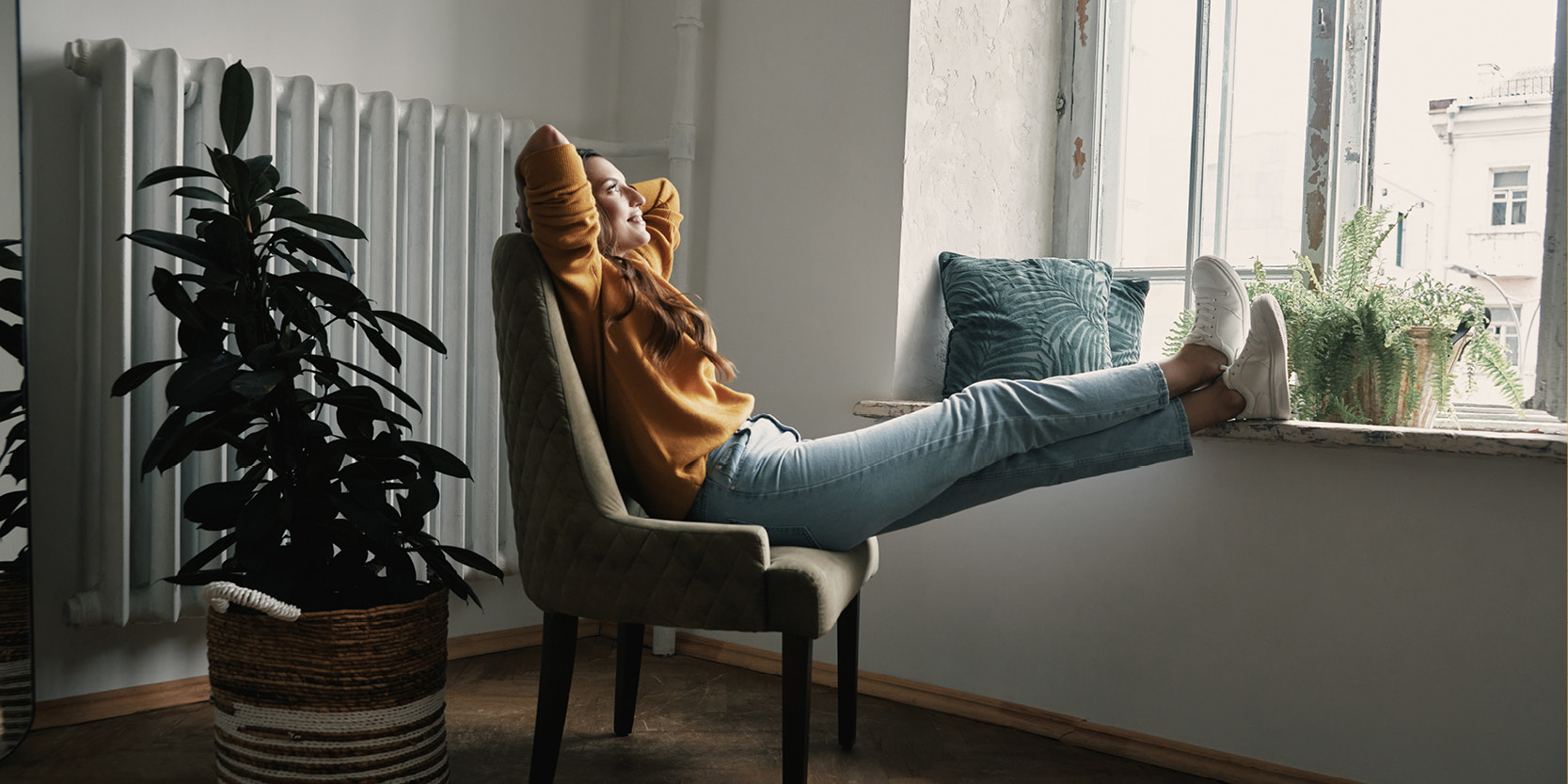 Ragazza seduta su una poltrona che si rilassa davanti alla finestra con gambe appoggiate a davanzale