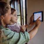 Mamma che tiene la figlia in braccio mentre sistemano il termostato smart