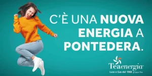 Immagine promozionale di Teaenergia. A sinistra, una giovane donna con un maglione arancione salta gioiosamente su uno sfondo acquamarina, con un'espressione energica. A destra, il testo bianco grande in maiuscolo dice: 'C'È UNA NUOVA ENERGIA A PONTEDERA.'. In basso a destra, c'è il logo di Teaenergia con l'icona a ventaglio stilizzata e il testo 'Luce e Gas dal 1908 gruppo Tea'.